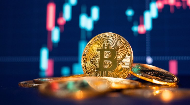 The picture of Bitcoin token in the forefront with a candle chart in the background.