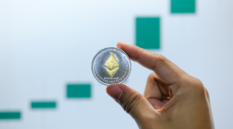 Ethereum token holded in two fingers with a upward green chart in the background, shutterstock