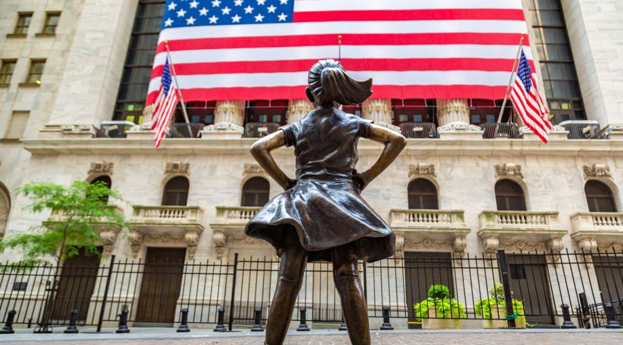 Fearless Girl Statue looking up at New York Stock Exchange building at Wall Street