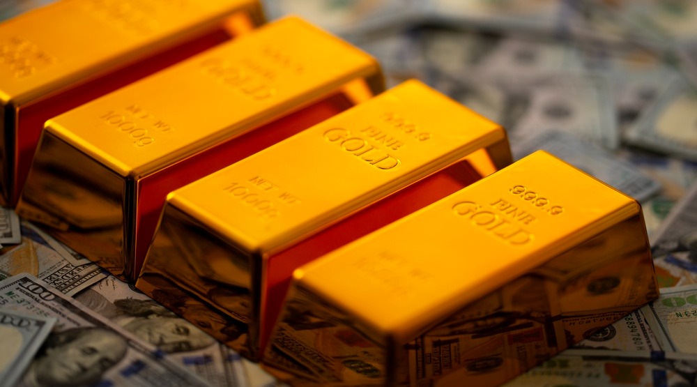Four gold bars laying one to each other on the stack of US dollars