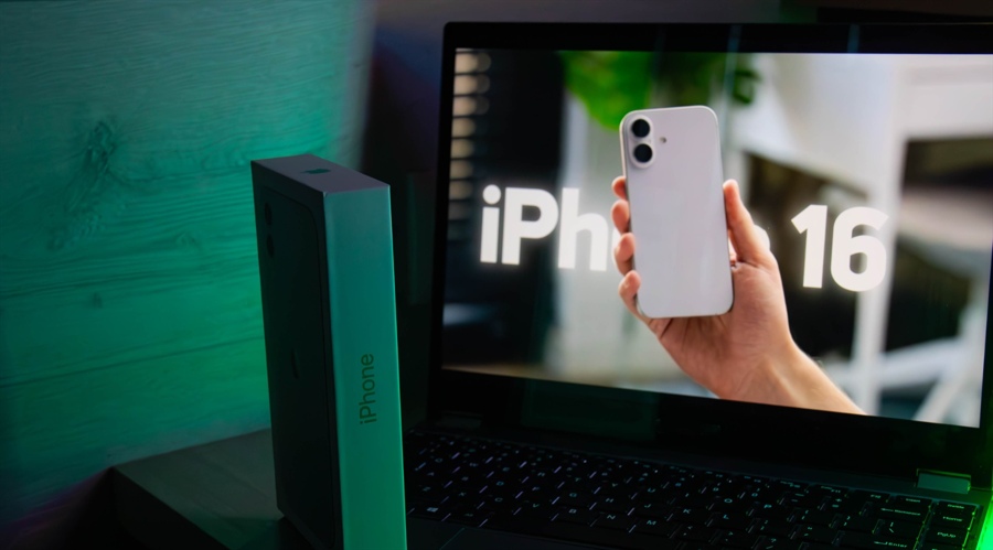 Apple iPhone 16 held in front of a laptop screen with its box nearby