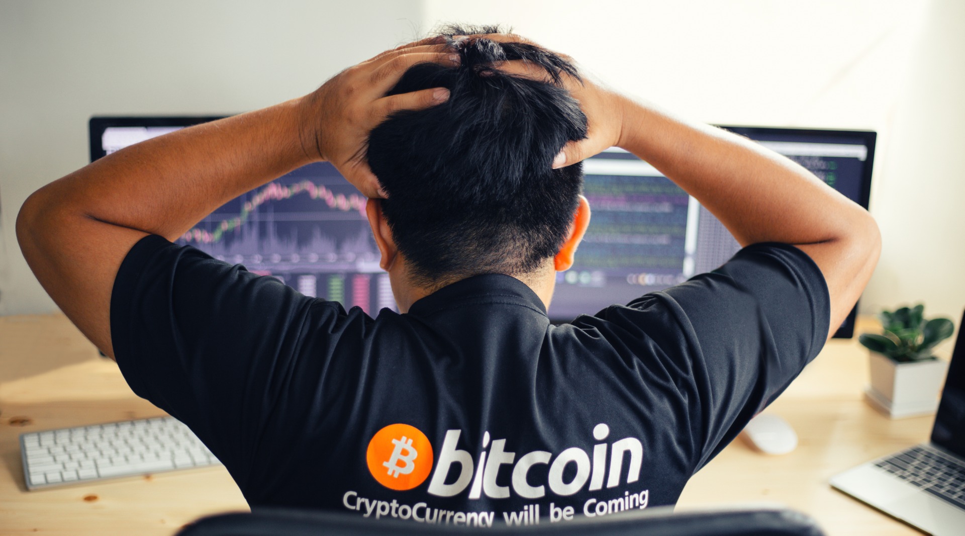 Man with Bitcoin logo on his t-shirt looking scared at the falling Bitcoin price charts