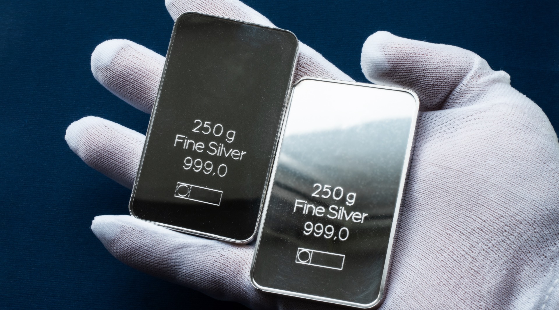 Two silver bars in the hand, dressed in a white protective glove. On a dark blue background